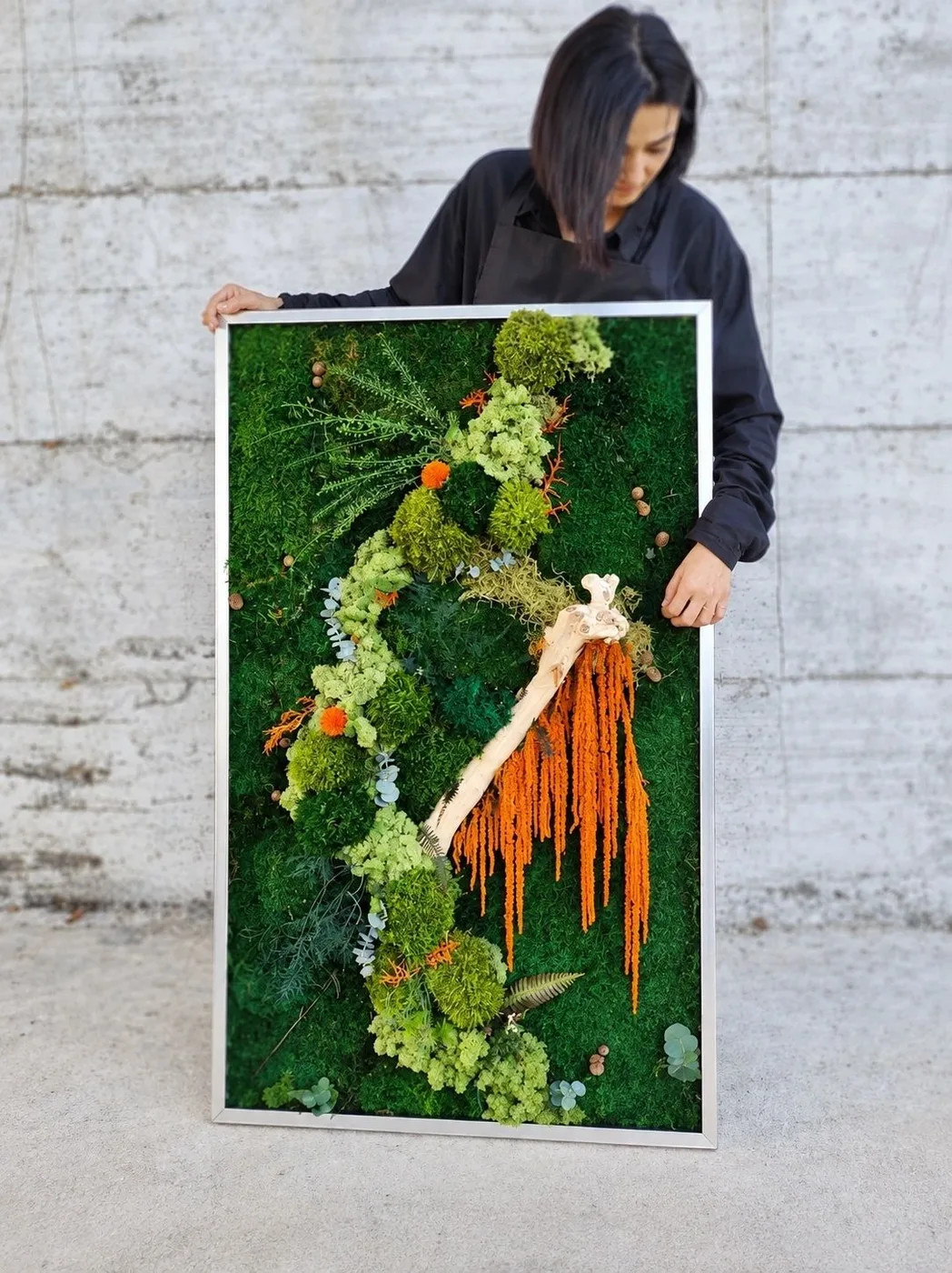 A person holding a large framed botanical composition in the MOSSY MOSS public gallery